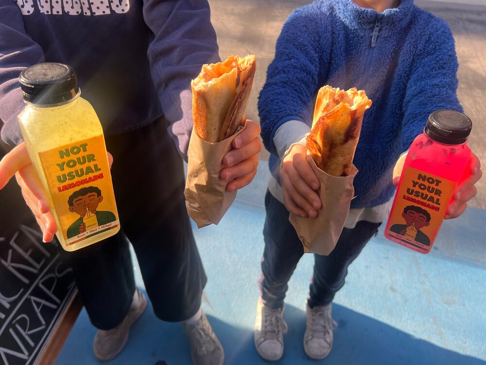 Two kids holding out wraps and lemonades