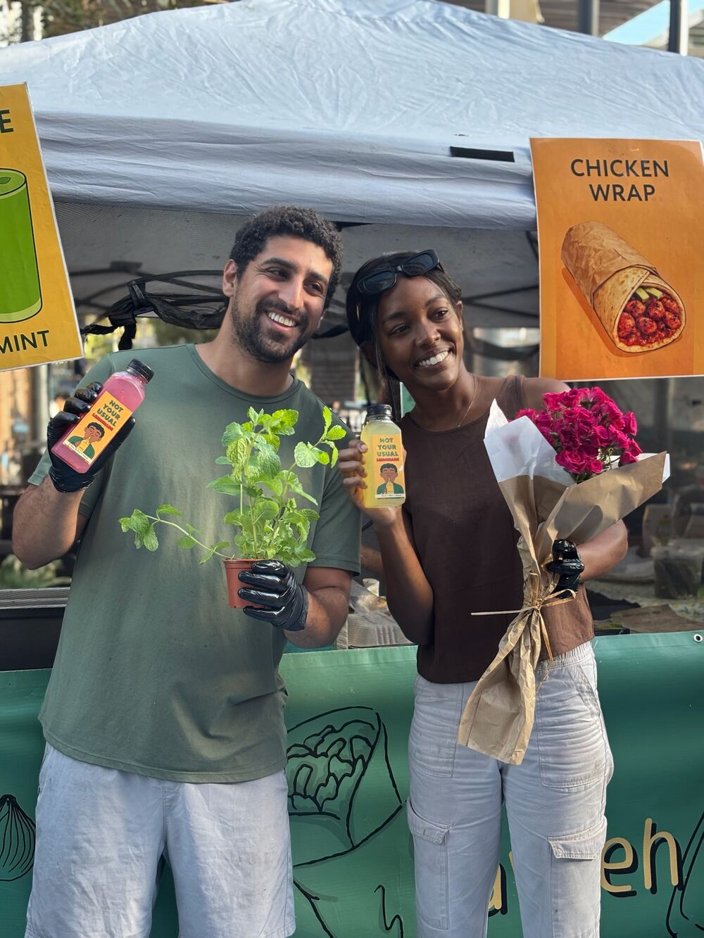 Two smiling team members at the Tawleh booth holding lemonades, fresh mint and roses